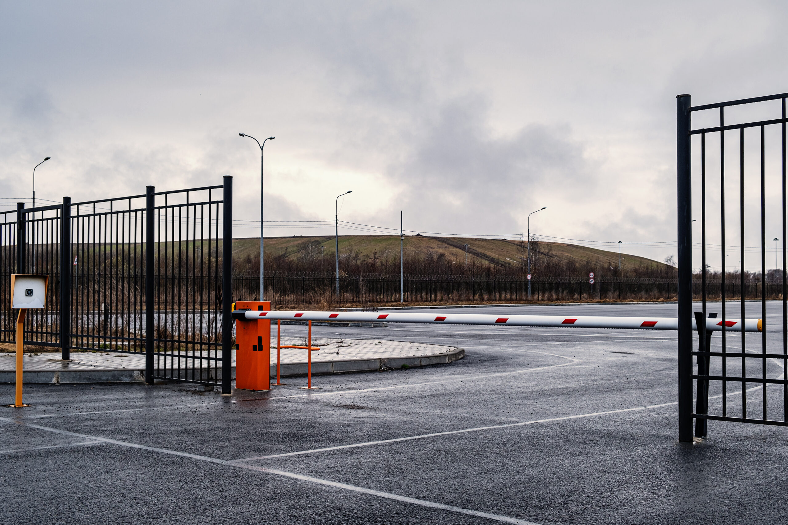Automatic barrier of orange color with a white stripe and red warning stripes, for the entry of cars. Entrance to the car factory parking lot